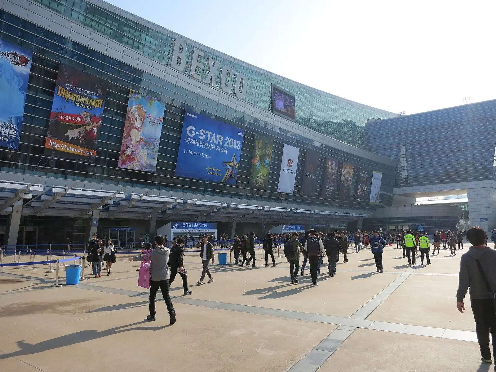 Visitors on the plaza outside BEXCO in Busan with game banners on the facade