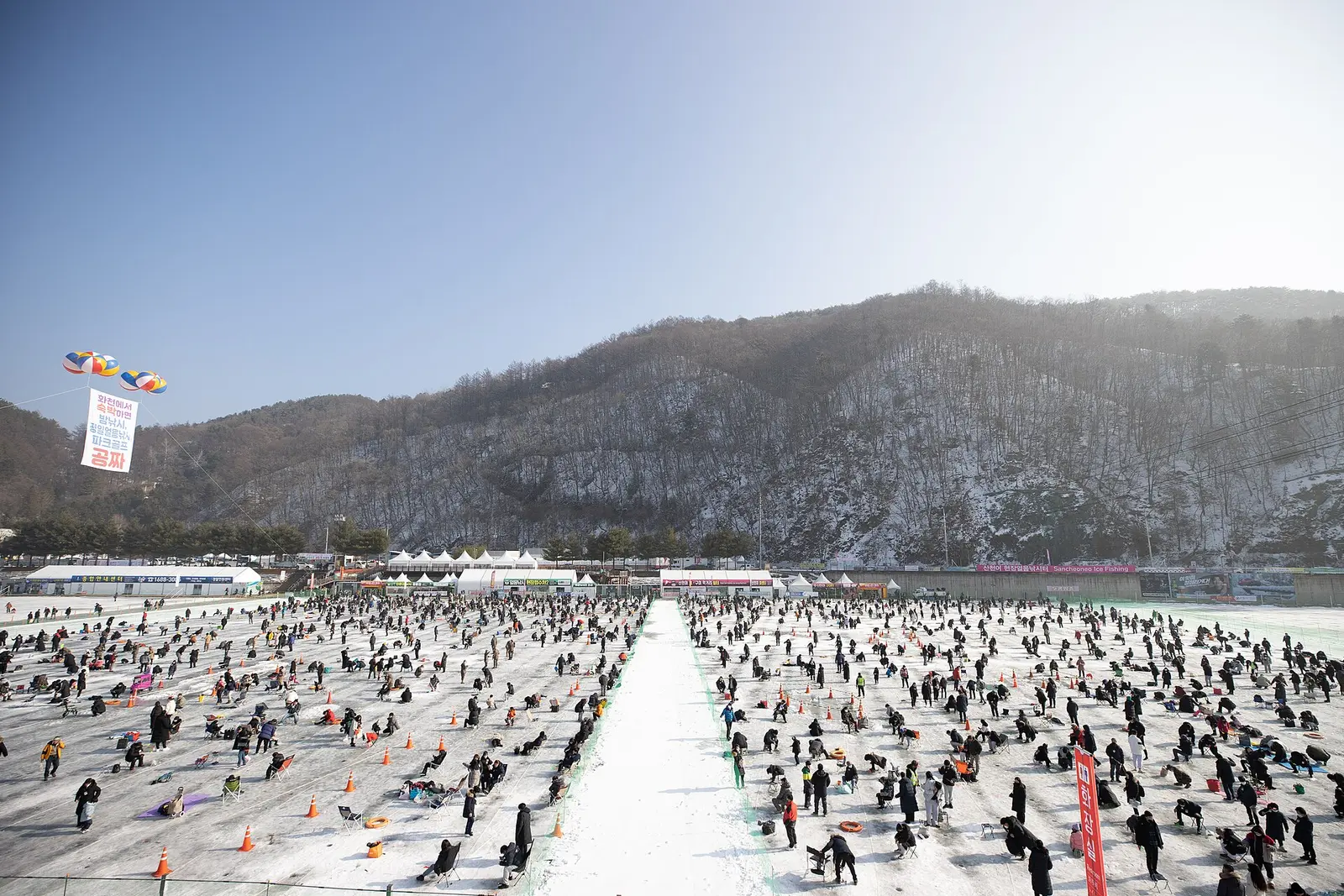 Crowds ice fishing on the frozen Hwacheon stream with mountains behind